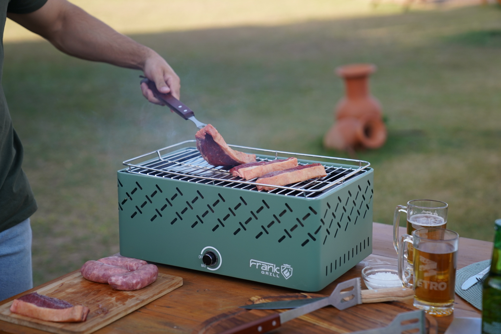 Fotografia das Churrasqueiras Frank Grill sendo utilizadas por um grupo de pessoas para preparar um churrasco no jardim, demonstrando seu uso doméstico.
