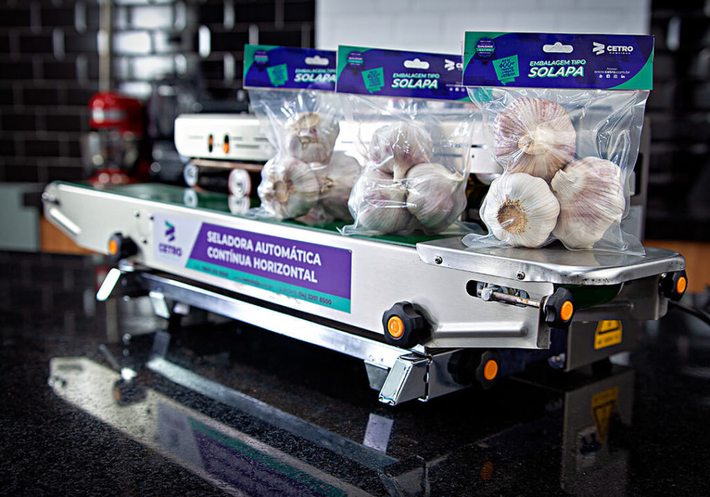 Fotografia de uma Seladora Automática da Cetro representando os processos de inovação de embalagens por meio da apresentação de pacotes de alho desenvolvidos com o apoio do maquinário.
