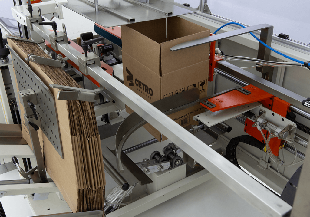 Close de um equipamento da linha de Montadoras de Caixas da Cetro em processos de molde de uma embalagem de papelão.