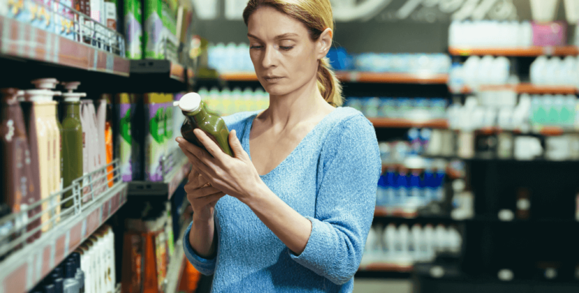 Fotografia de uma mulher de pele branca observando uma garrafa de suco em um corretor de supermercado – representando a importância de estar atento ao desperdício de alimentos.