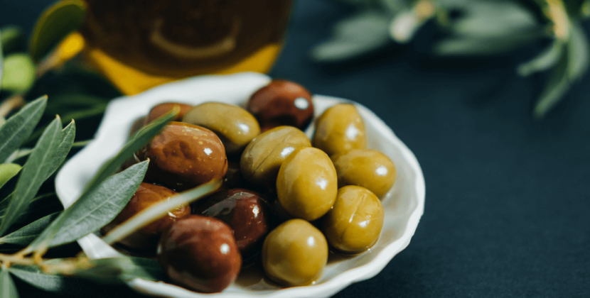 Registro de uma porção de azeitonas em um prato branco ao lado de um galho de oliveira – representando as oportunidades de otimização de uma embalagem de azeitona.