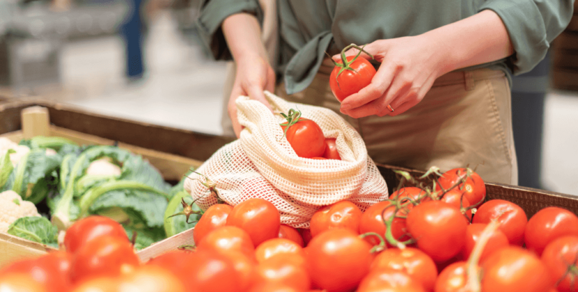 Fotografia de um consumidor consciente com uma sacola ecológica selecionando tomates em um supermercado.