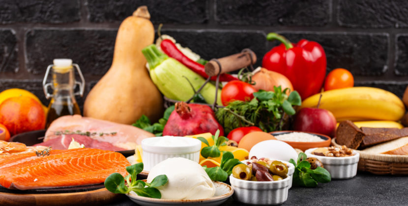 Imagem de diferentes alimentos, peças de carne, peixe, frutas, queijo, azeitonas e vegetais, representando o mercado alimentício