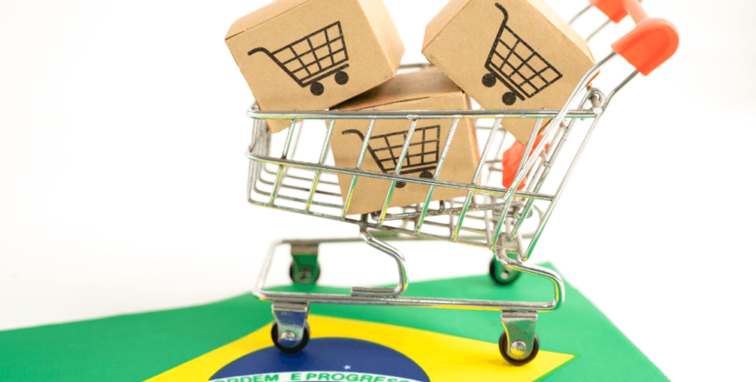 Foto de um carrinho de compras em miniatura com caixas de papelão sobre a bandeira do Brasil, representando as oportunidades do mercado brasileiro.