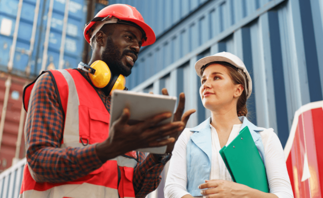 Imagem de um homem e uma mulher com equipamentos de proteção perto de contêiners, representando o ato de exportar produtos.