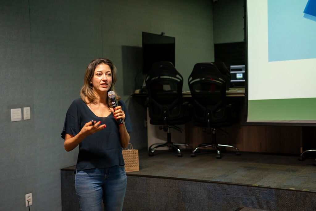 Palestrante em um auditório segurando um microfone e utilizando uma tela para projetar as imagens da apresentação sobre o Novembro Azul aos colaboradores Cetro.