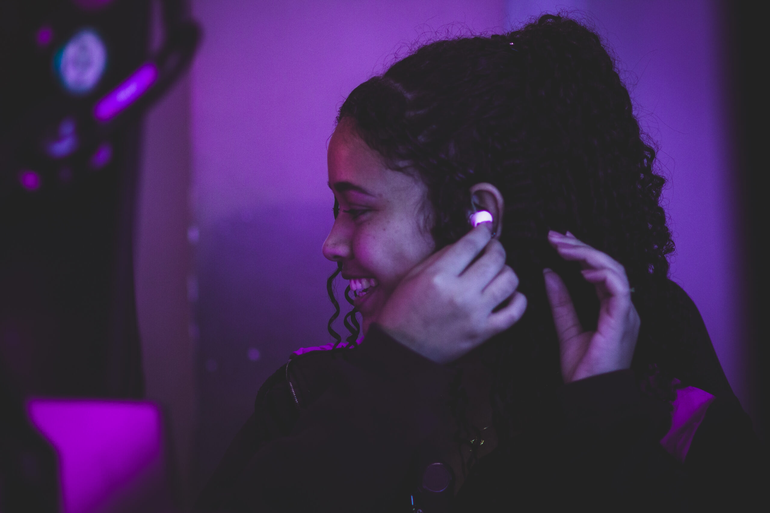 Fotografia de uma colaboradora sorrindo e colocando um fone de ouvido bluetooth em sua orelha.