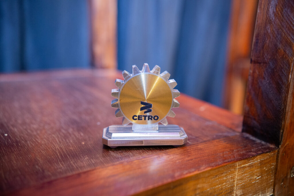 Fotografias dos colaboradores da Cetro com o troféu no evento e uma imagem do troféu do SENAI sobre uma mesa de madeira.