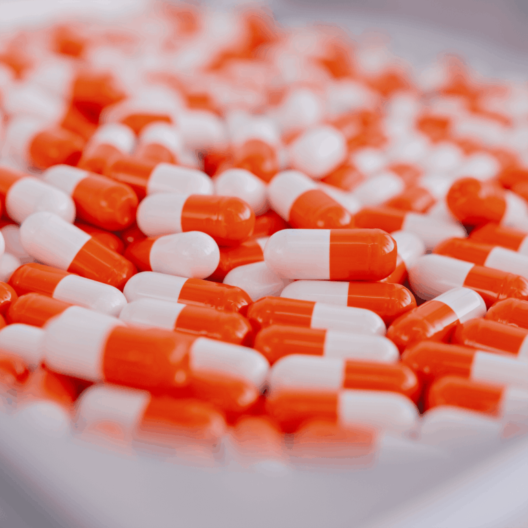 Fotografia de medicamentos em cápsulas brancas e laranjas em uma bandeja.