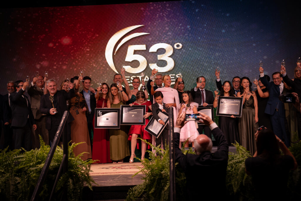 Fotografias da família de Léo Mello recebendo o prêmio no palco e dos colaboradores da Cetro e seus cônjuges que compareceram ao evento.