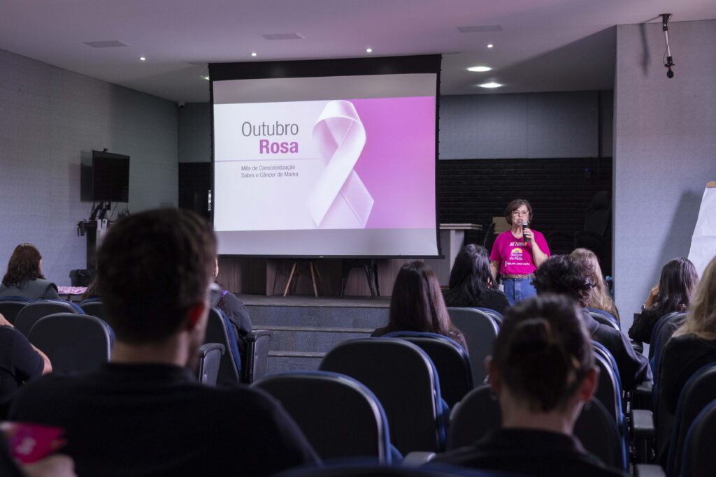 Fotografia dos colaboradores da Cetro assistindo à palestra sobre Outubro Rosa e das representantes do Grupo Amigas do Peito fazendo a apresentação.