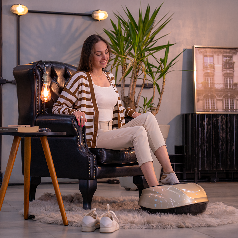Fotografias de uma mulher utilizando o Massageador para Pés da Linha C-RES7 da Cetro sentada em uma poltrona preta em uma sala confortável e apertando os botões do aparelho.