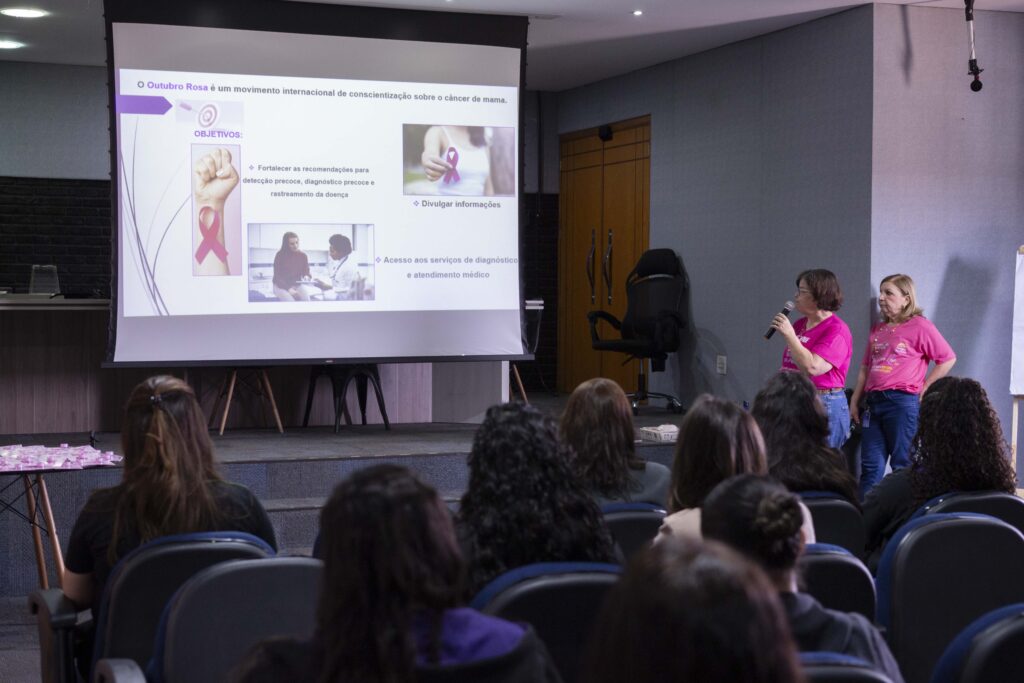 Fotografia dos colaboradores da Cetro assistindo à palestra sobre Outubro Rosa e das representantes do Grupo Amigas do Peito fazendo a apresentação.