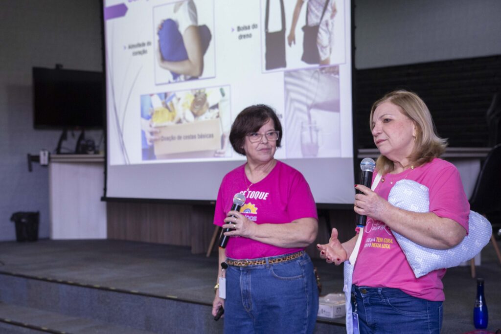 Fotografia dos colaboradores da Cetro assistindo à palestra sobre Outubro Rosa e das representantes do Grupo Amigas do Peito entregando folhetos aos participantes.