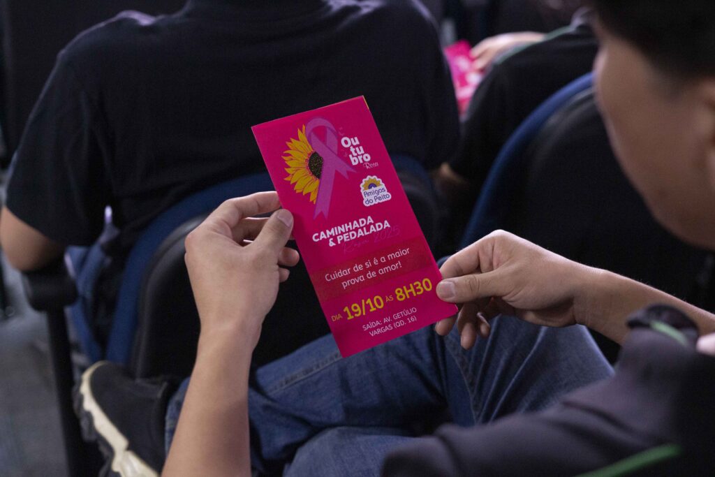 Fotografia dos colaboradores da Cetro assistindo à palestra sobre Outubro Rosa e das representantes do Grupo Amigas do Peito entregando folhetos aos participantes.