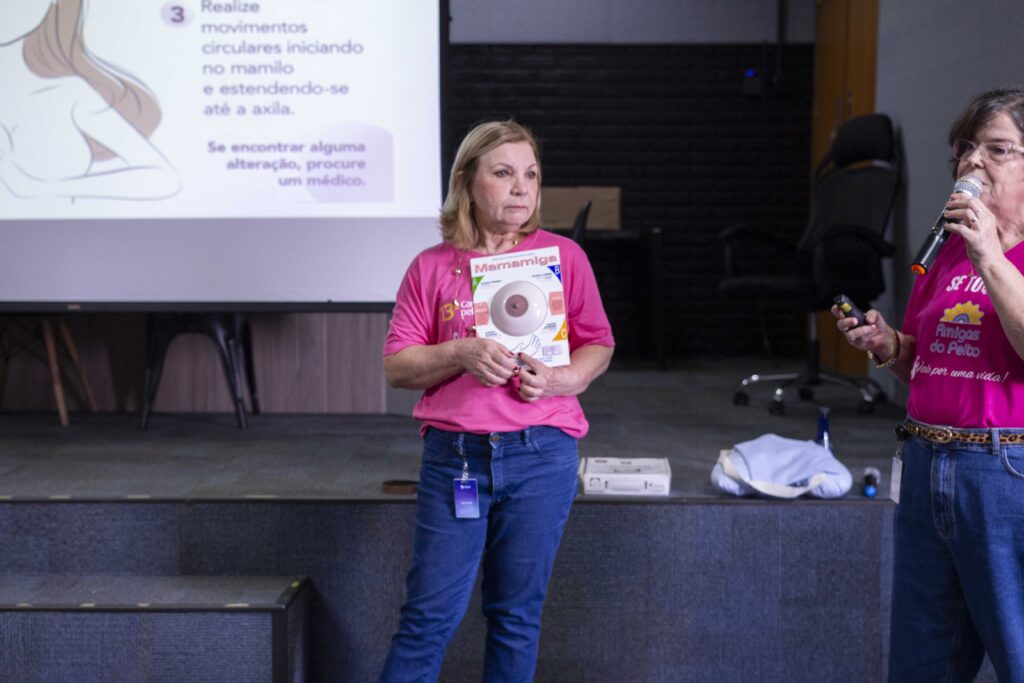 Fotografia dos colaboradores da Cetro assistindo à palestra sobre Outubro Rosa e das representantes do Grupo Amigas do Peito mostrando o modelo didático “Mamamiga”.