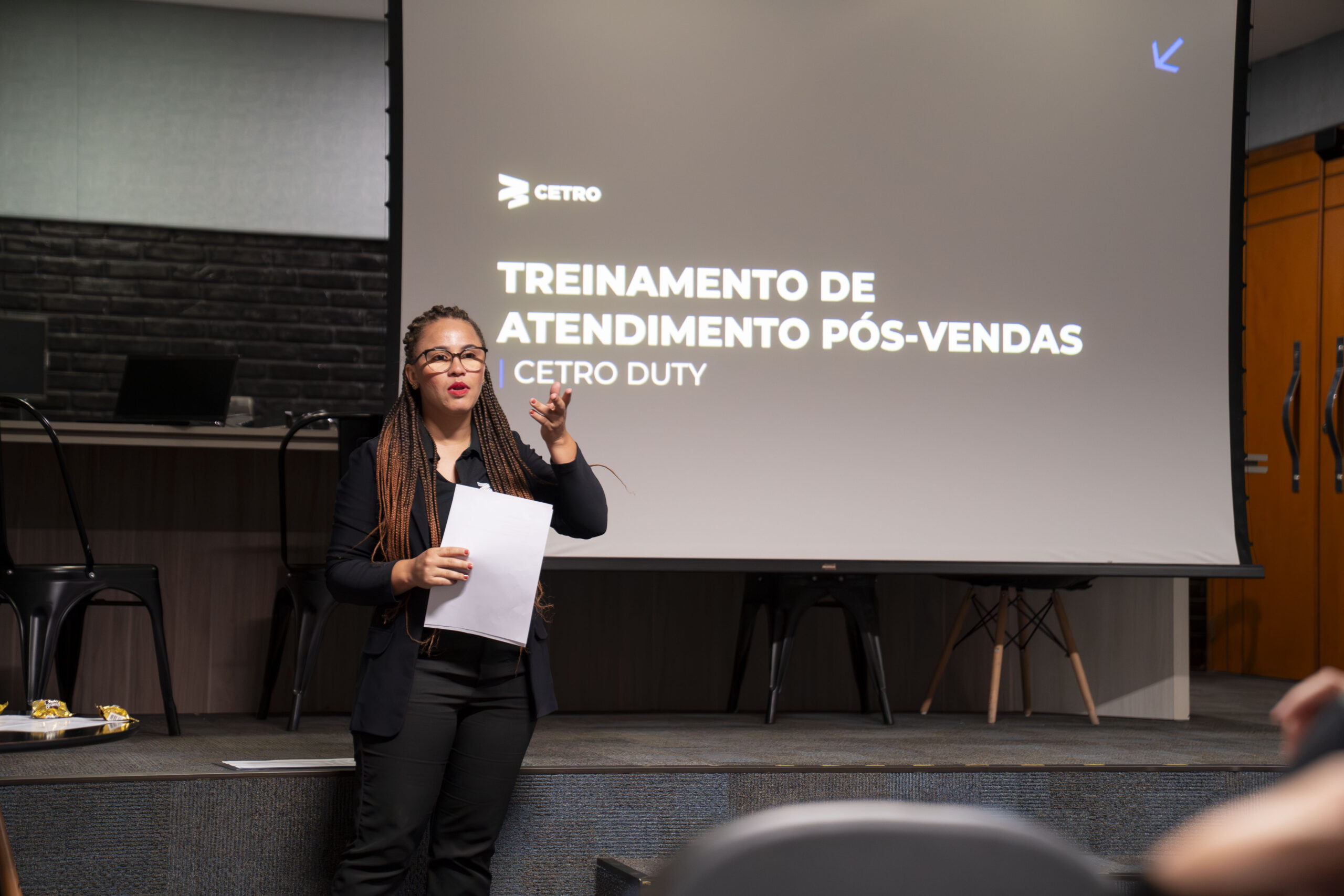 Fotografias dos alimentos expostos na mesa para o coffee break e de uma colaboradora Cetro em frente ao telão de apresentação do treinamento.