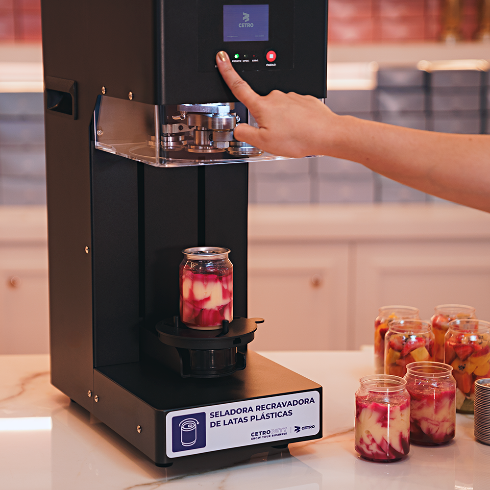 Fotografias da Seladora Recravadora de Latas Plásticas Semiautomática CCBM S-100 CS T da Cetro e de latas com sobremesas seladas por ela.