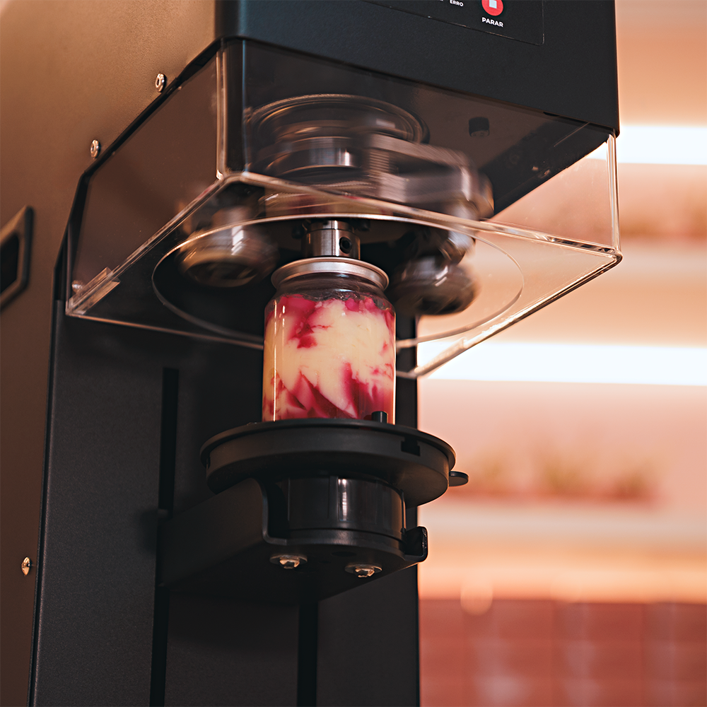 Fotografias da Seladora Recravadora de Latas Plásticas Semiautomática CCBM S-100 CS T da Cetro e de latas com sobremesas seladas por ela.