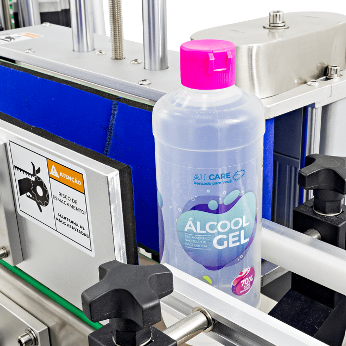 Fotografias da Rotuladora Automática de Frascos Cilíndricos de Bancada CALM T e de um frasco de álcool em gel rotulado na esteira da máquina.