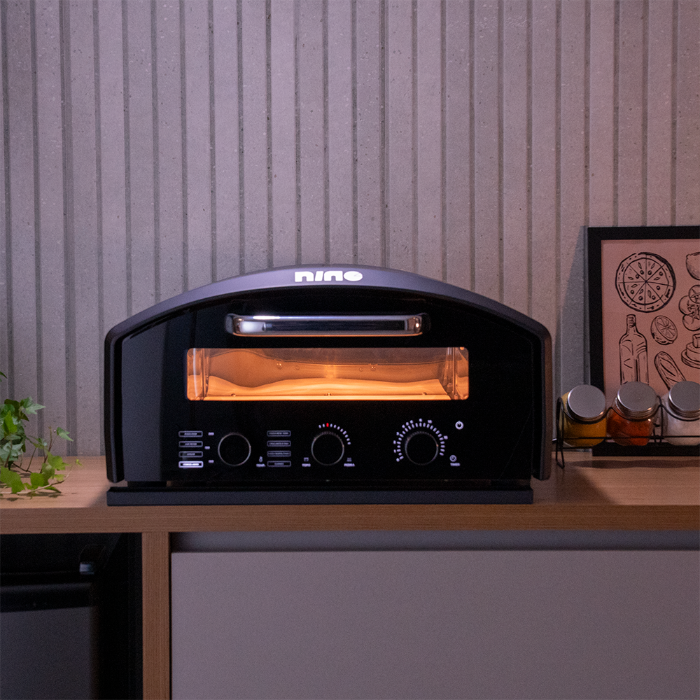 Fotografias do Forno de Pizza Nino Elétrico com Pedra Quadrada CFBM PO-330 S E da Cetro assando uma pizza napolitana sobre uma bancada.