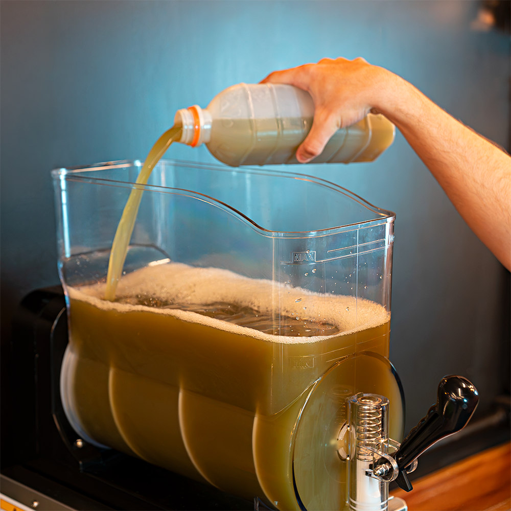 Uma Máquina de Raspadinha e Bebidas Congeladas Slush da Cetro Duty sendo abastecida com produto e uma raspadinha verde decorada com uma fatia de limão em um copo de plástico.